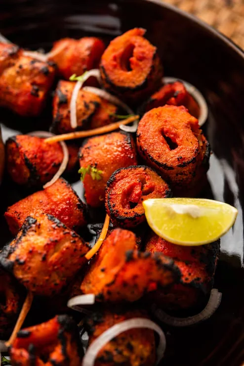 Charred tandoori tikka pieces with sliced onion and a lemon wedge, straight off the skewer