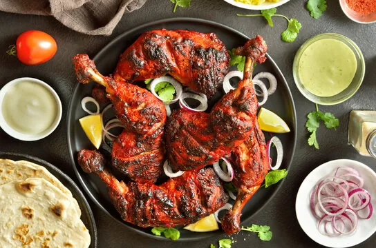 Tandoori chicken on a black platter with onion, lemon and chutneys